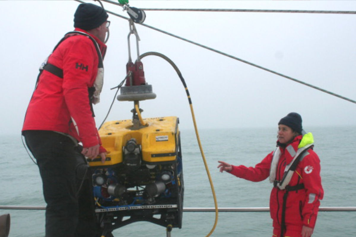 Two Sea Rangers at sea using a pully system to lower an underwater robot (ROV) into the sea to record a seaweed farm under the ocean surface.
