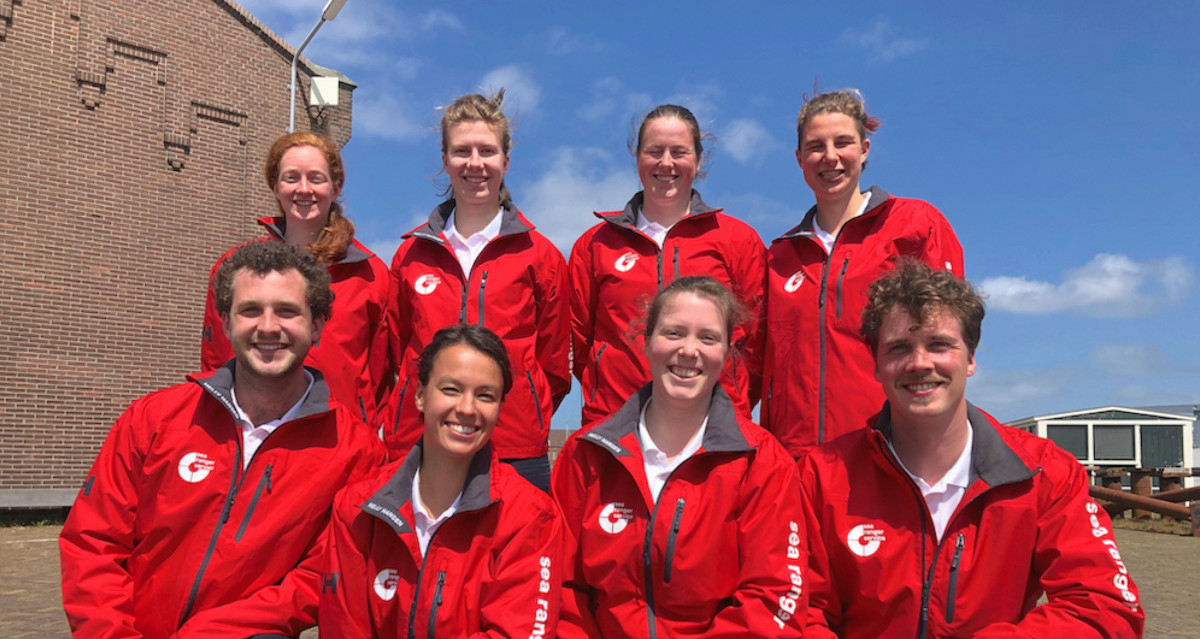 A team of eight Sea Rangers in red Sea Ranger uniforms posed in two rows of four. There are four female Sea Rangers standing up in the back row, and two male and two female Sea Rangers kneeling down in the front row. All are smiling and look happy.