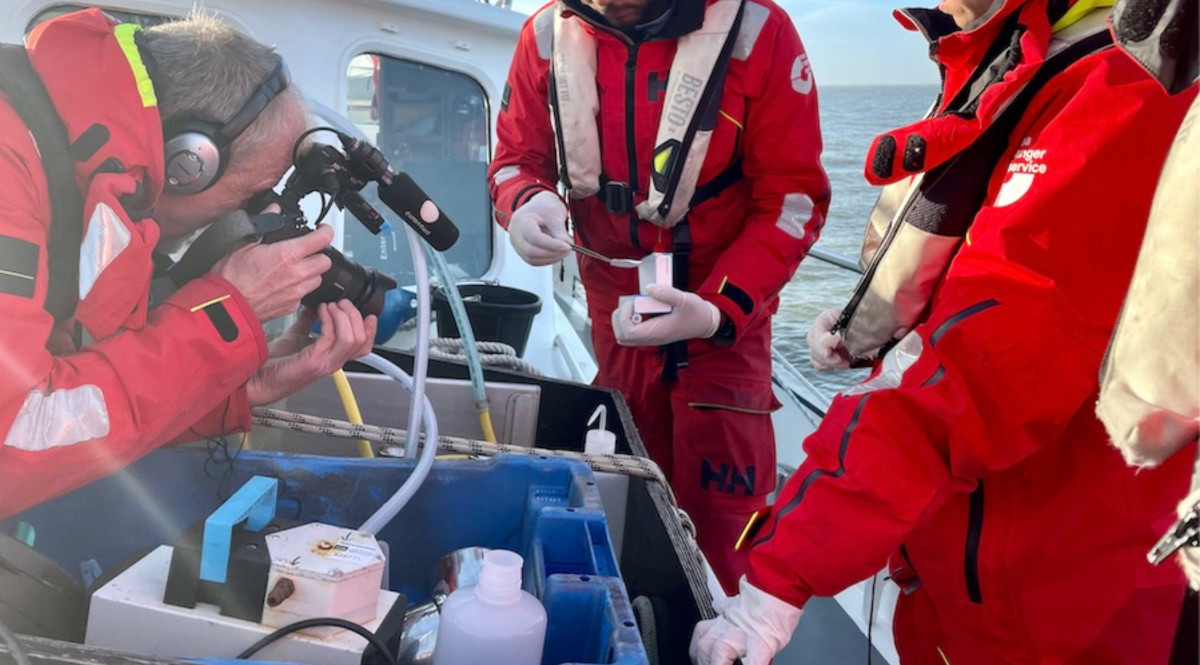 Three Sea Rangers are onboard a ship, out to sea. One Sea Ranger is filming the conservation work that the other two Sea Rangers are doing.