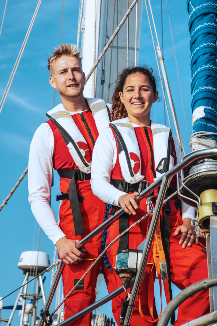 A male and female Sea Ranger, both dressed in red Sea Ranger uniforms, pose at the front of a ship.