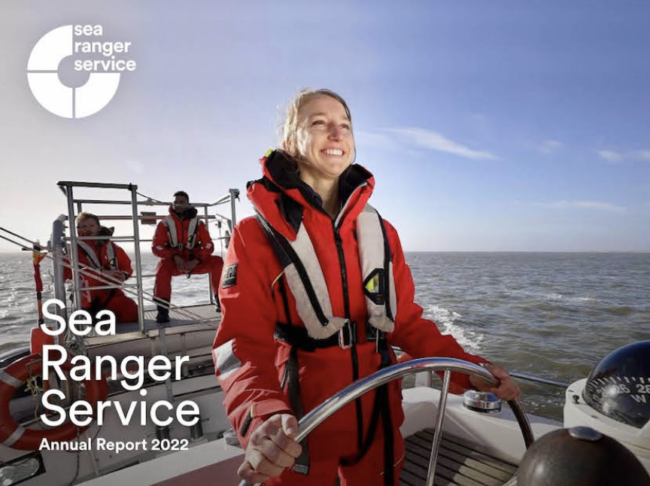 Front cover of the Sea Ranger Service annual report 2022. Image is a female Sea Ranger steering a sailing ship on a calm sea.
